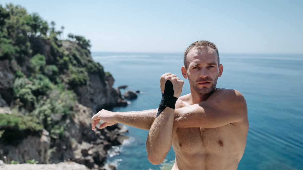 Athletic man performing outdoor stretches by picturesque seaside cliffs under the sun.